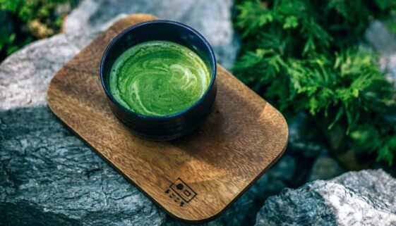 Green Tea in a black cup on arock in a forest
