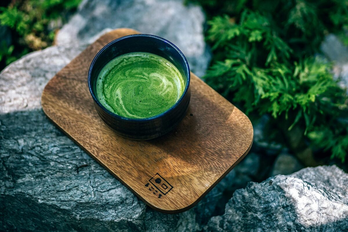 Green Tea in a black cup on arock in a forest